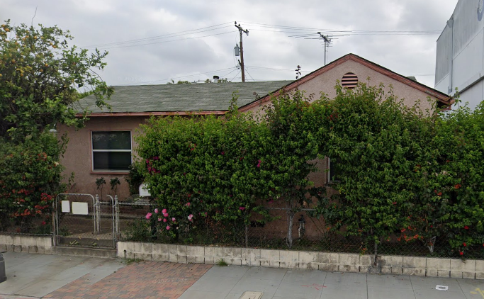 A house with a grey roof and a brown wall covered in green plants.